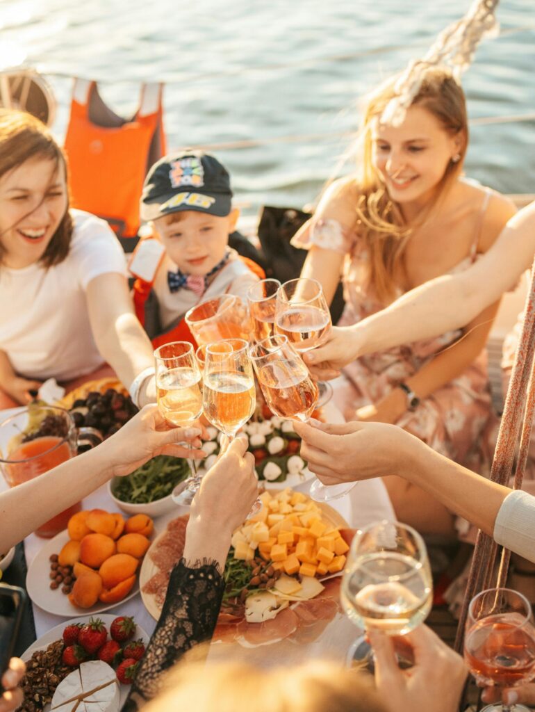 Group of friends enjoying a summer yacht party with drinks and a vibrant food spread.