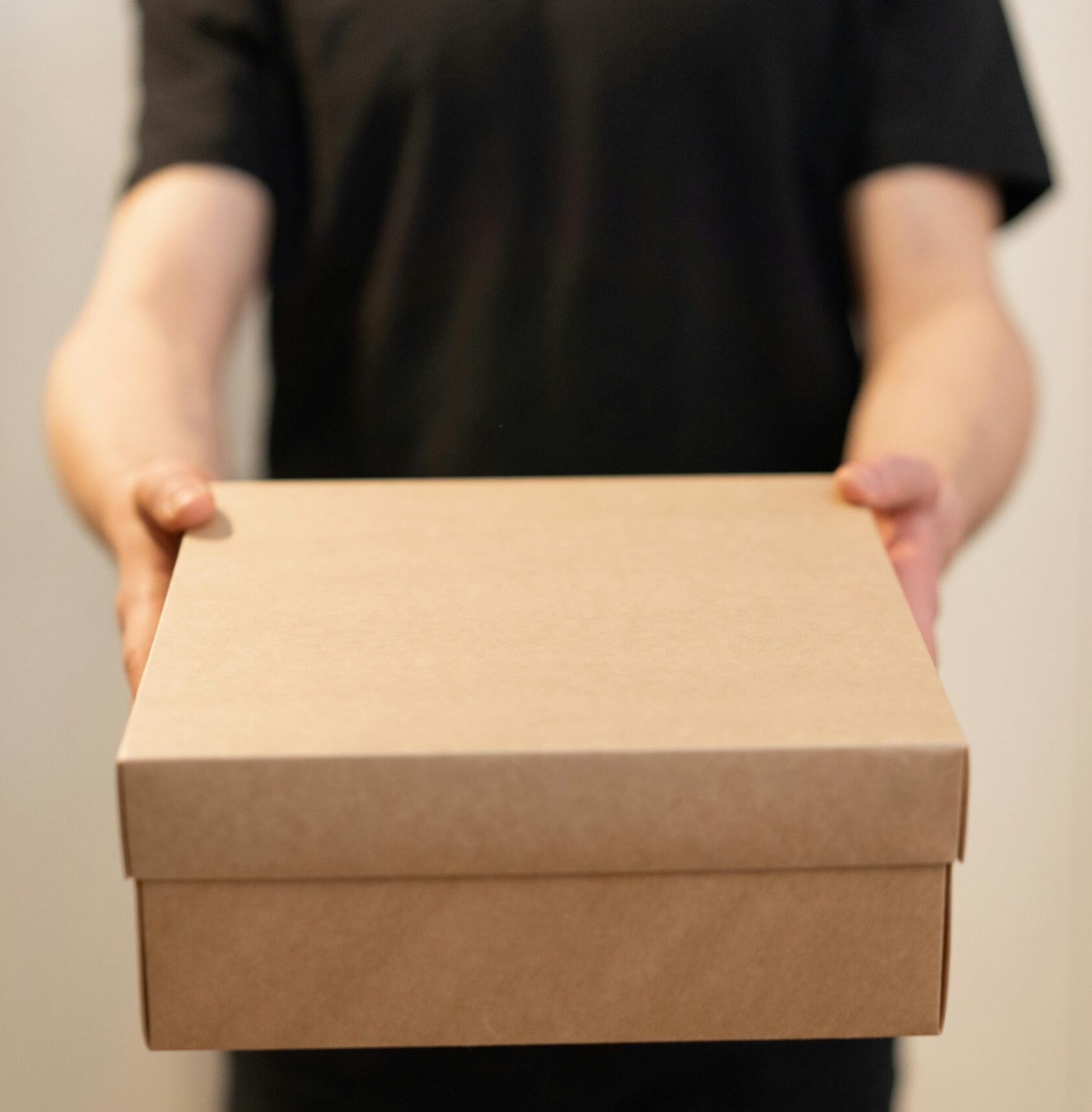 Close-up of a person holding a cardboard box, ideal for delivery service concepts.